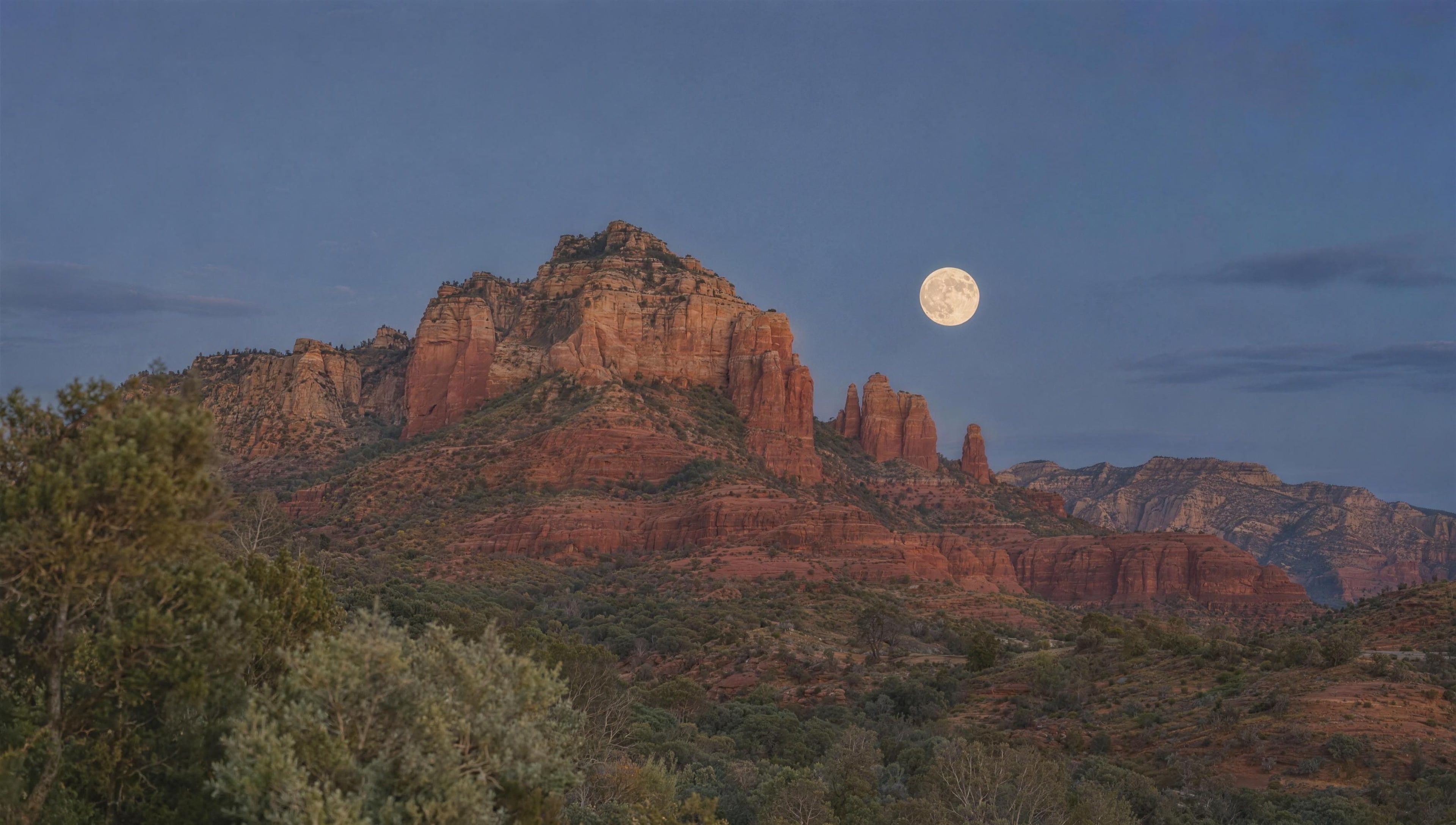 A red rock ridge in Sedona under a rising full moon at blue hour